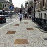 Op de foto is een trottoir naast een Amsterdamse straat te zien. Tussen de tegels van het troittoir zijn diverse koperkleurige tegels te zien, die deel moeten uitmaken van de Walk of Pride